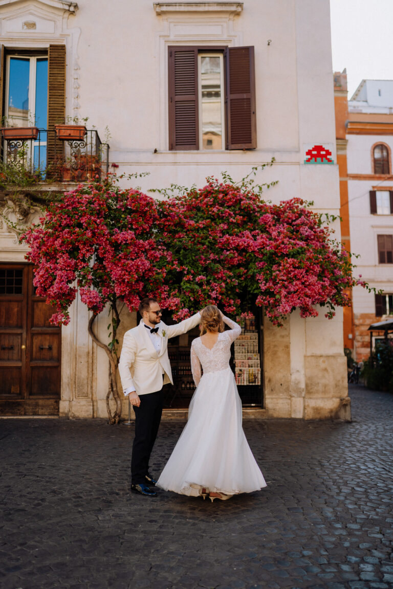 Bride and groom under blooming pink flowers in Rome, romantic street portrait.